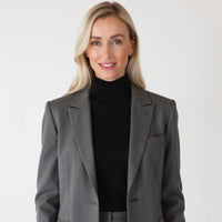 Caitlin Krumm wearing a gray blazer over a black turtleneck on a white background